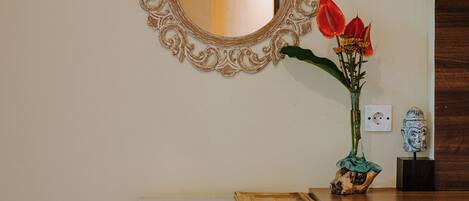 Un miroir avec un cadre orné, un vase rempli de fleurs rouges et une petite statue posée sur une console blanche.