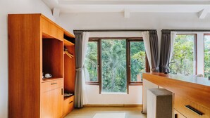 A modern kitchen with wooden cabinets, a countertop, and a view of lush greenery through large windows. - Dewangga Ubud (Ubud)