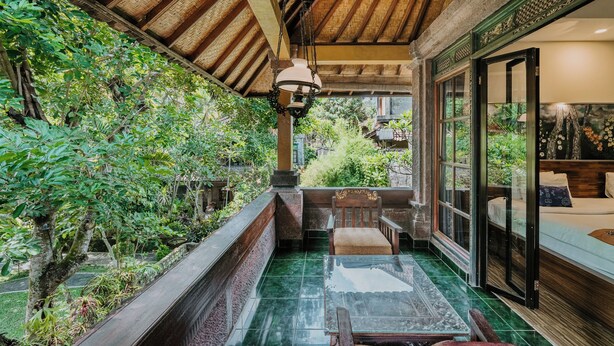 A covered balcony with a glass table and chairs, surrounded by lush greenery. - Dewangga Ubud (Ubud)