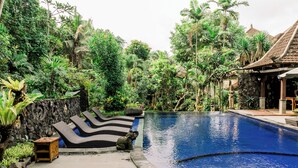 A serene pool area with lounge chairs, a stone wall, and lush tropical vegetation. - Dewangga Ubud (Ubud)