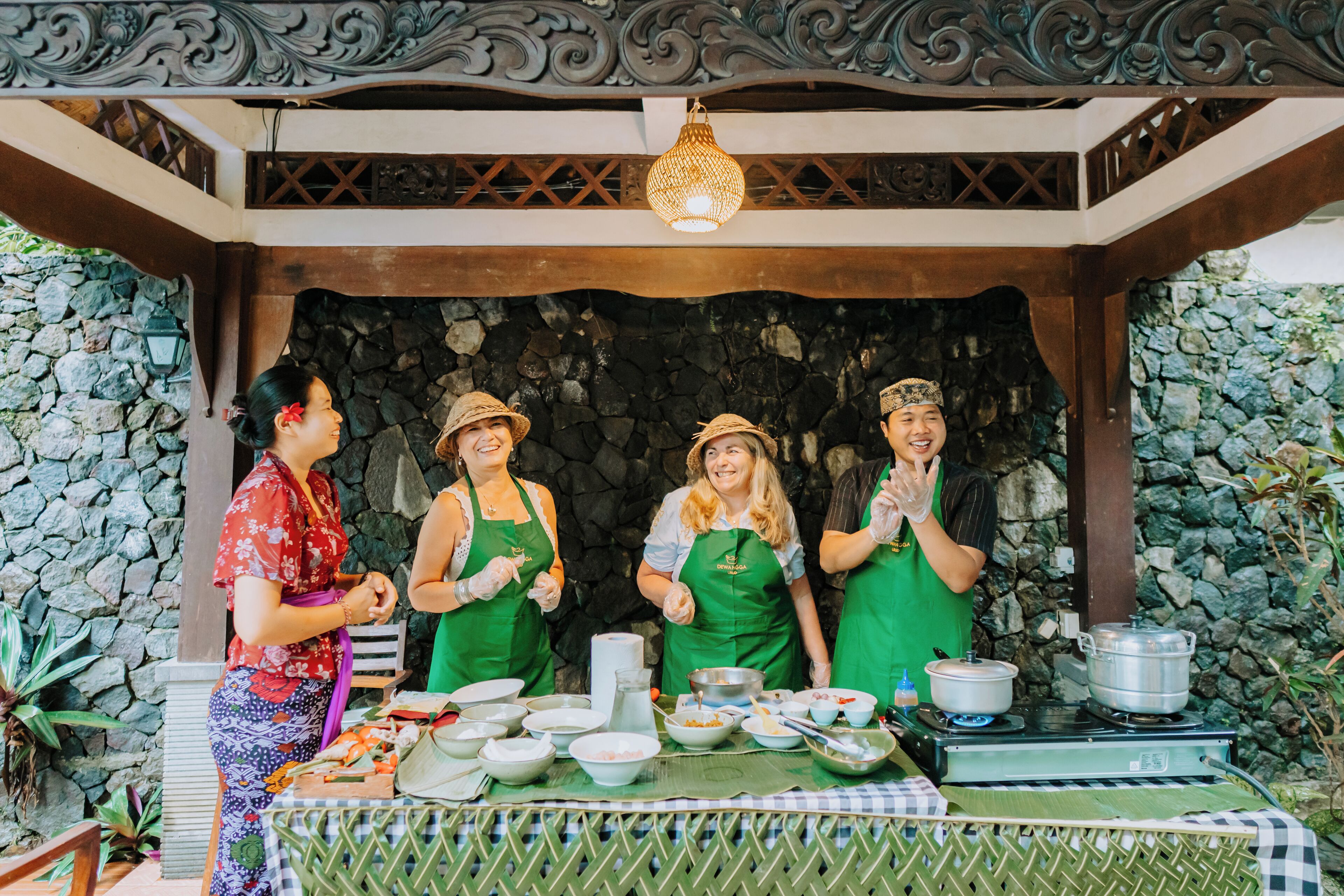 Four people in aprons standing in front of a cooking setup with pots and bowls.