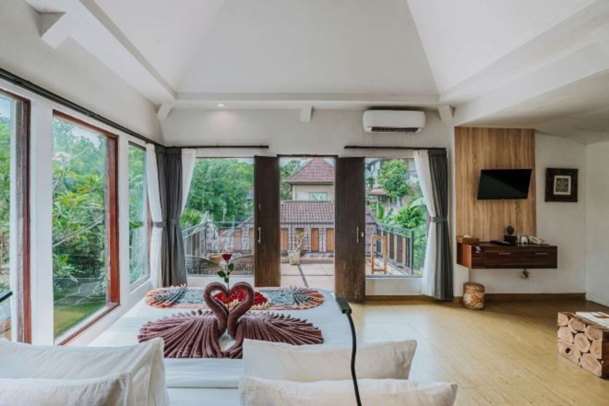 A spacious room with large windows, a flat-screen TV, and a wooden floor.