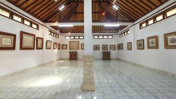 A spacious gallery with a high ceiling, tiled floor, and framed artworks on the walls.
