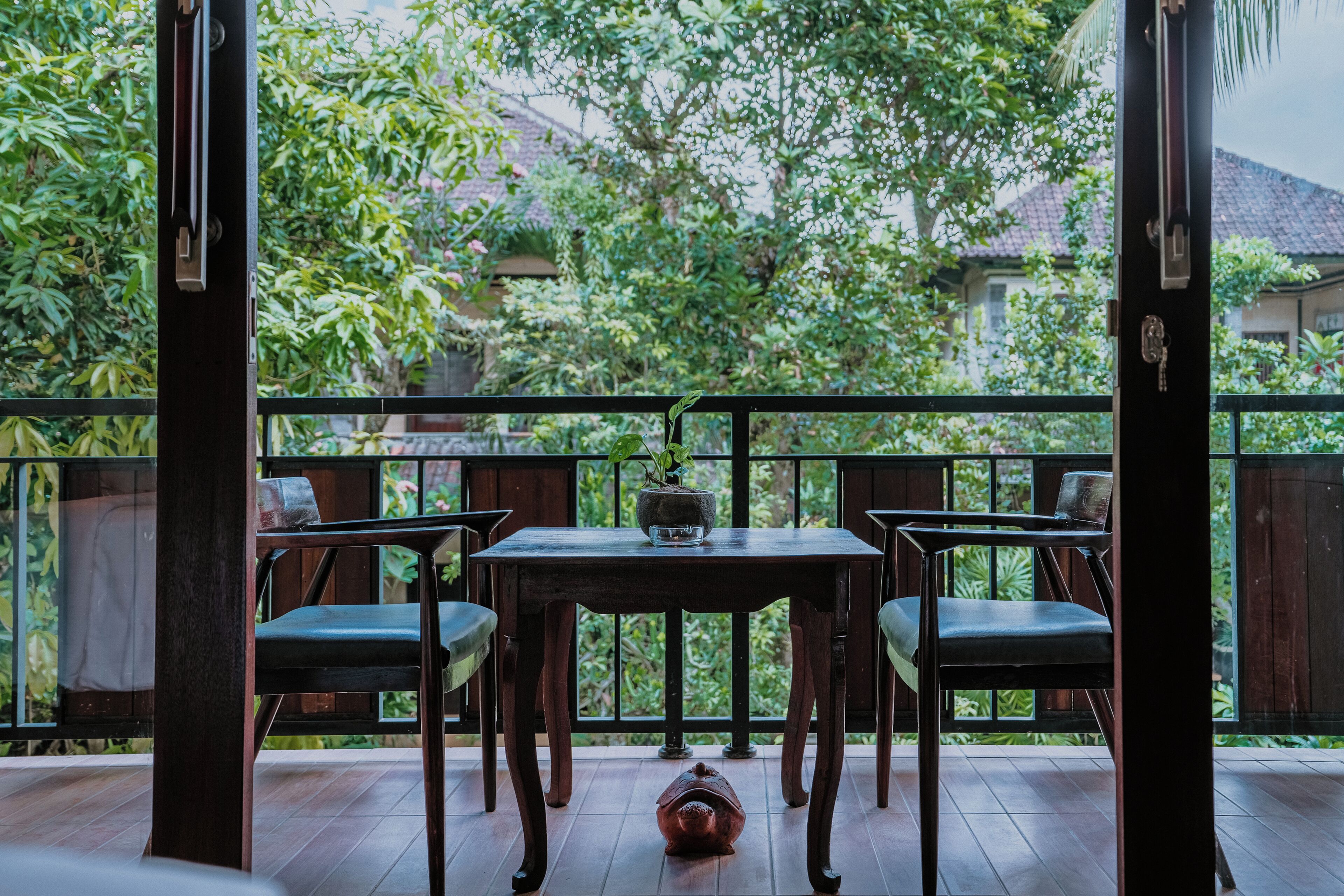 An outdoor patio with a wooden table and chairs, surrounded by a wooden fence and lush greenery.