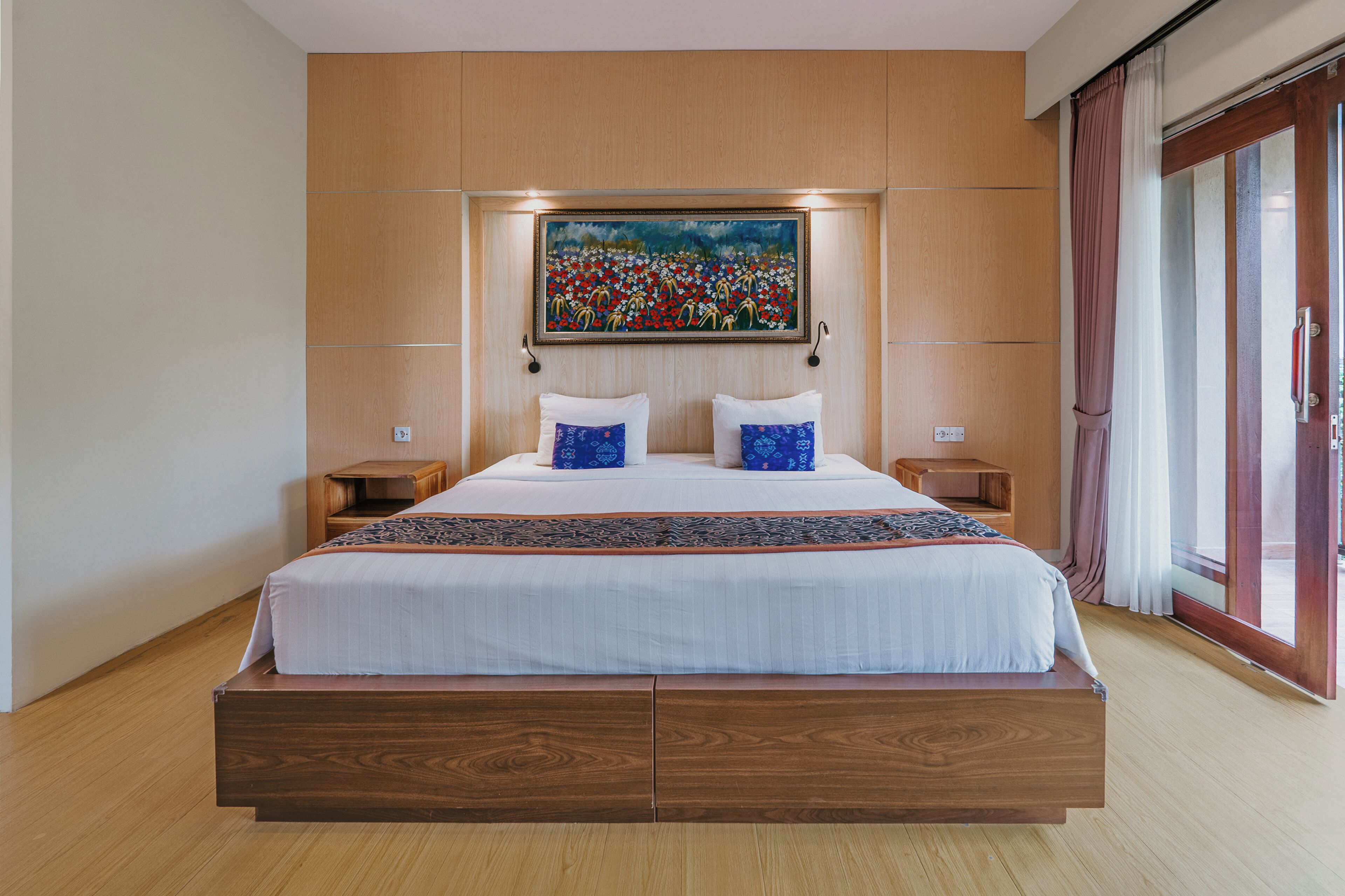 Ein modernes Hotelzimmer mit einem großen Bett, einem Holzkopfstück und einem Gemälde darüber.