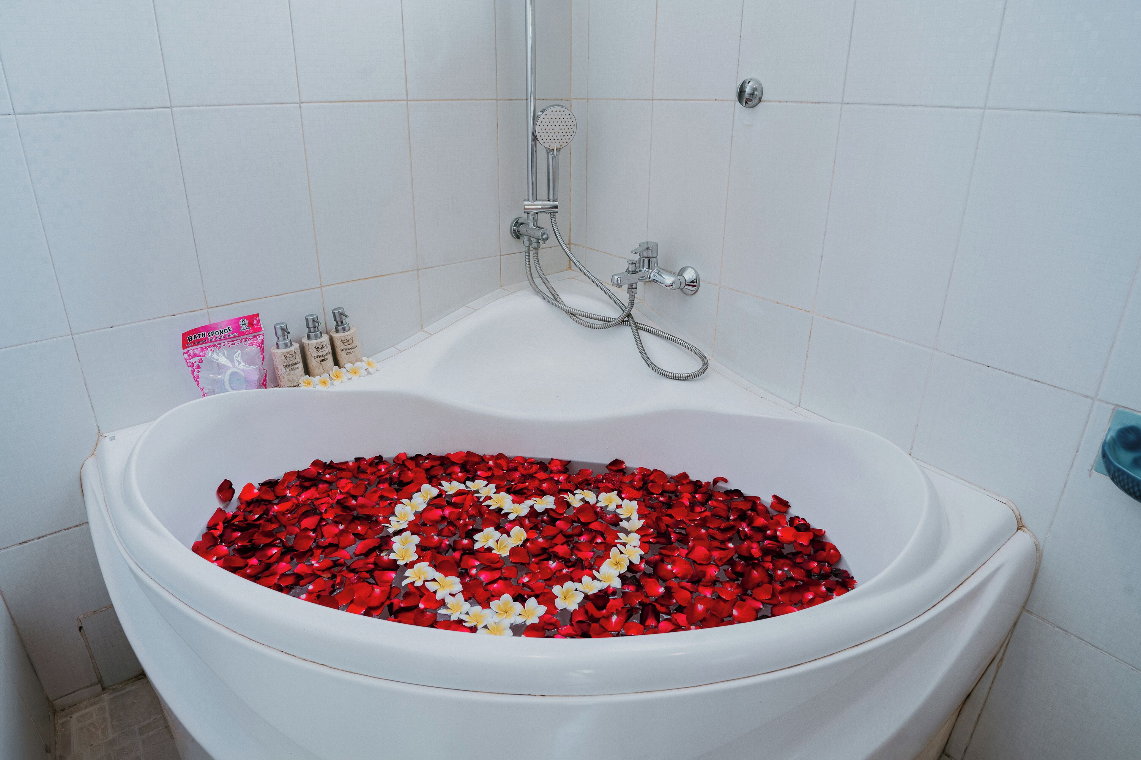A bathtub filled with water and rose petals, a showerhead, and a bottle of shampoo.