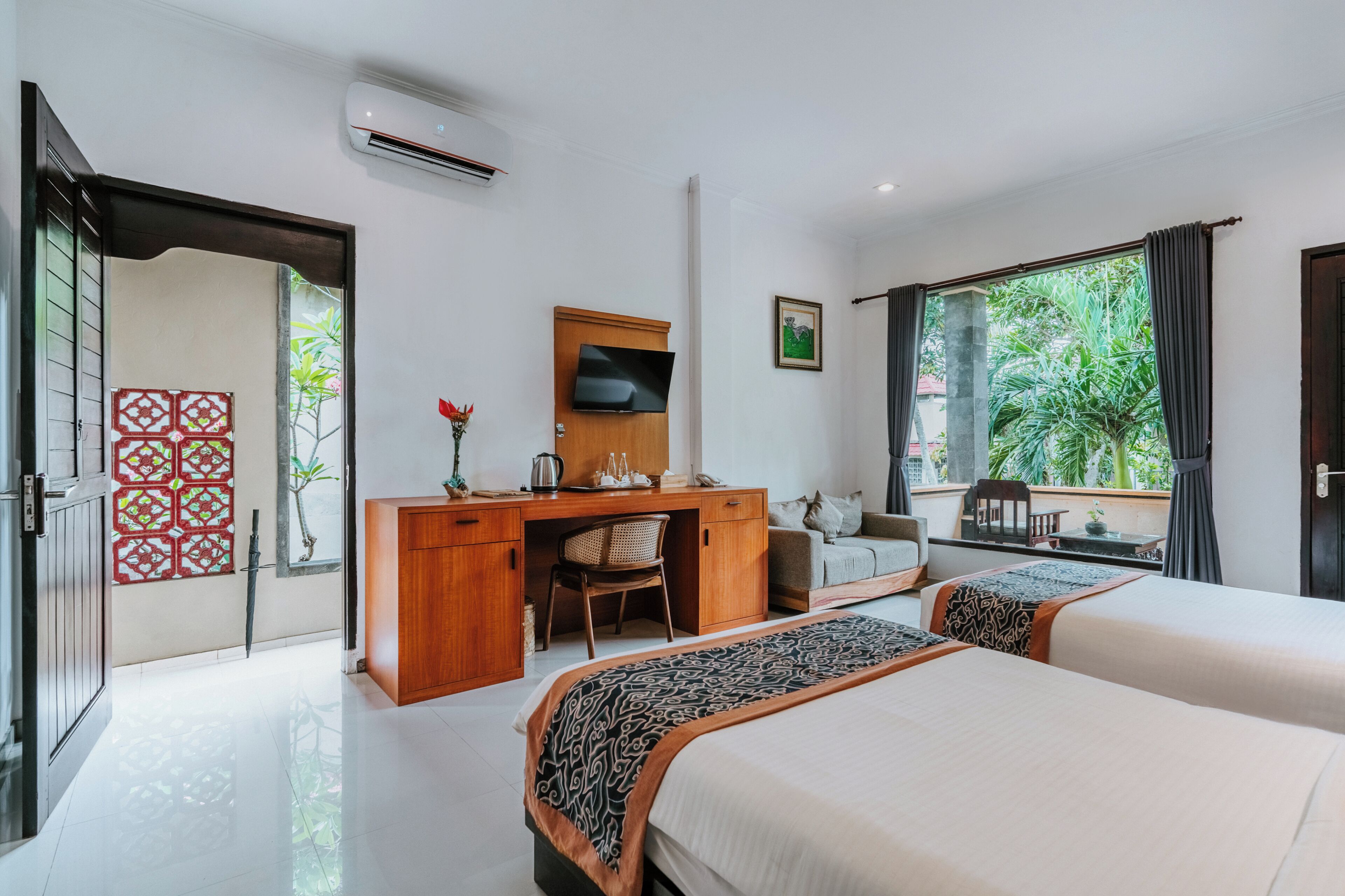 A modern hotel room with two beds, a desk, a TV, and a large window with a view of greenery.