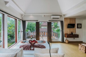 A spacious room with large windows, a bed with heart-shaped towels, a TV, and a wooden cabinet.