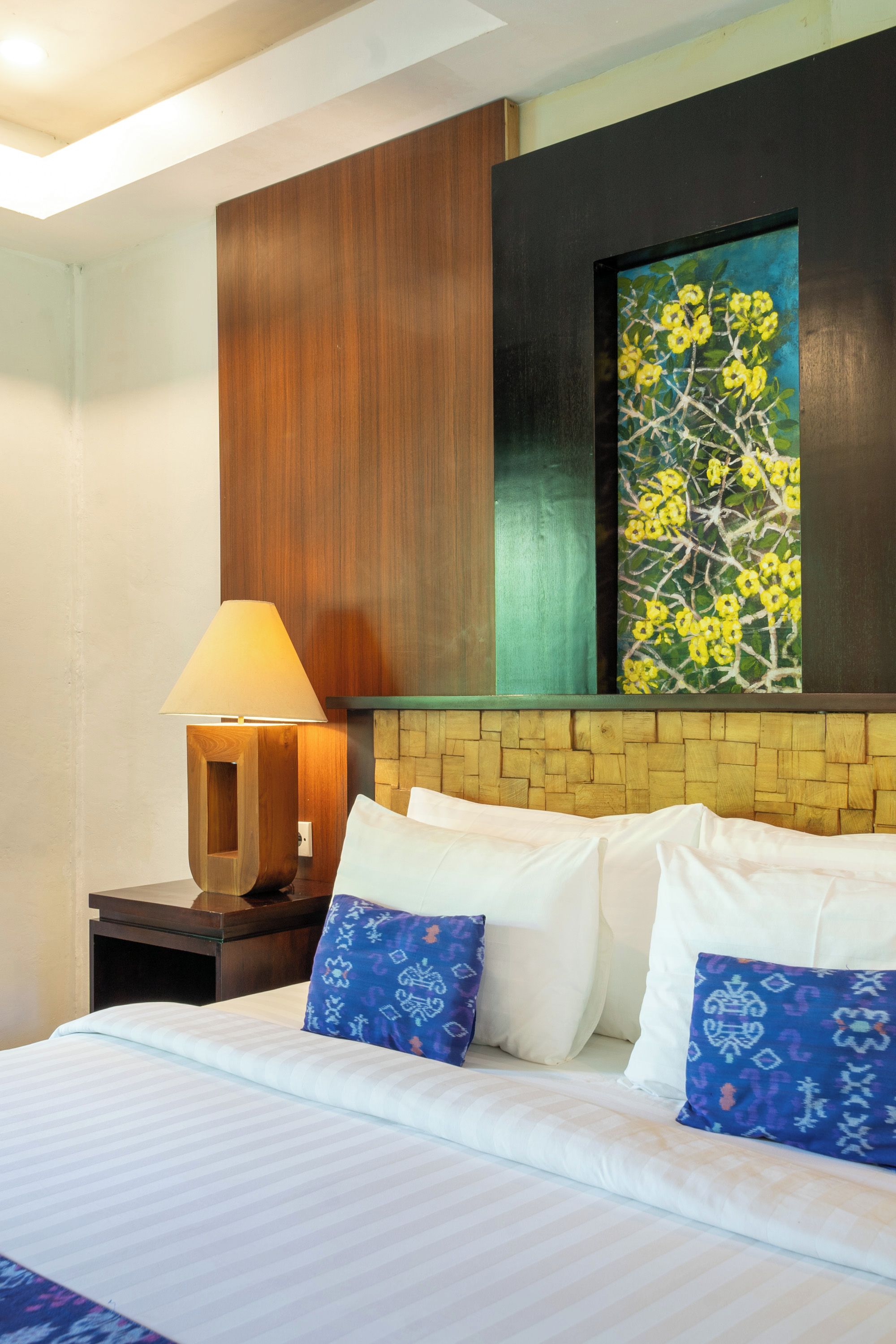 Une chambre d’hôtel comprenant un lit, des oreillers, une table de chevet, une lampe et une œuvre d’art murale.