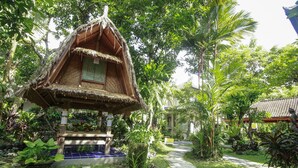 A traditional thatched-roof structure with a tiled blue floor, surrounded by lush greenery and a paved pathway. - Dewangga Ubud (Ubud)