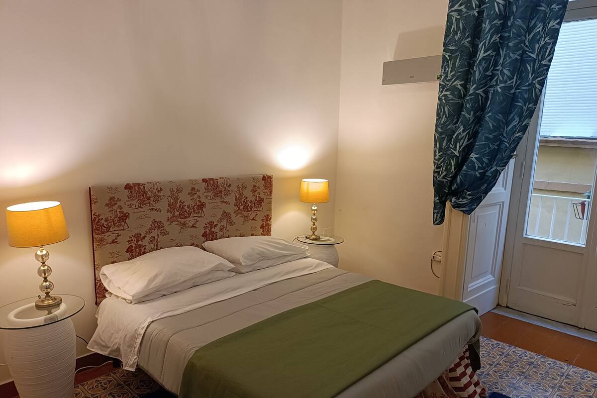 A neatly made bed with a floral headboard, two bedside lamps, and a green throw blanket.