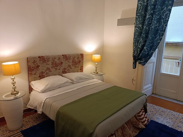 A neatly made bed with a floral headboard, two bedside lamps, and a green throw blanket.