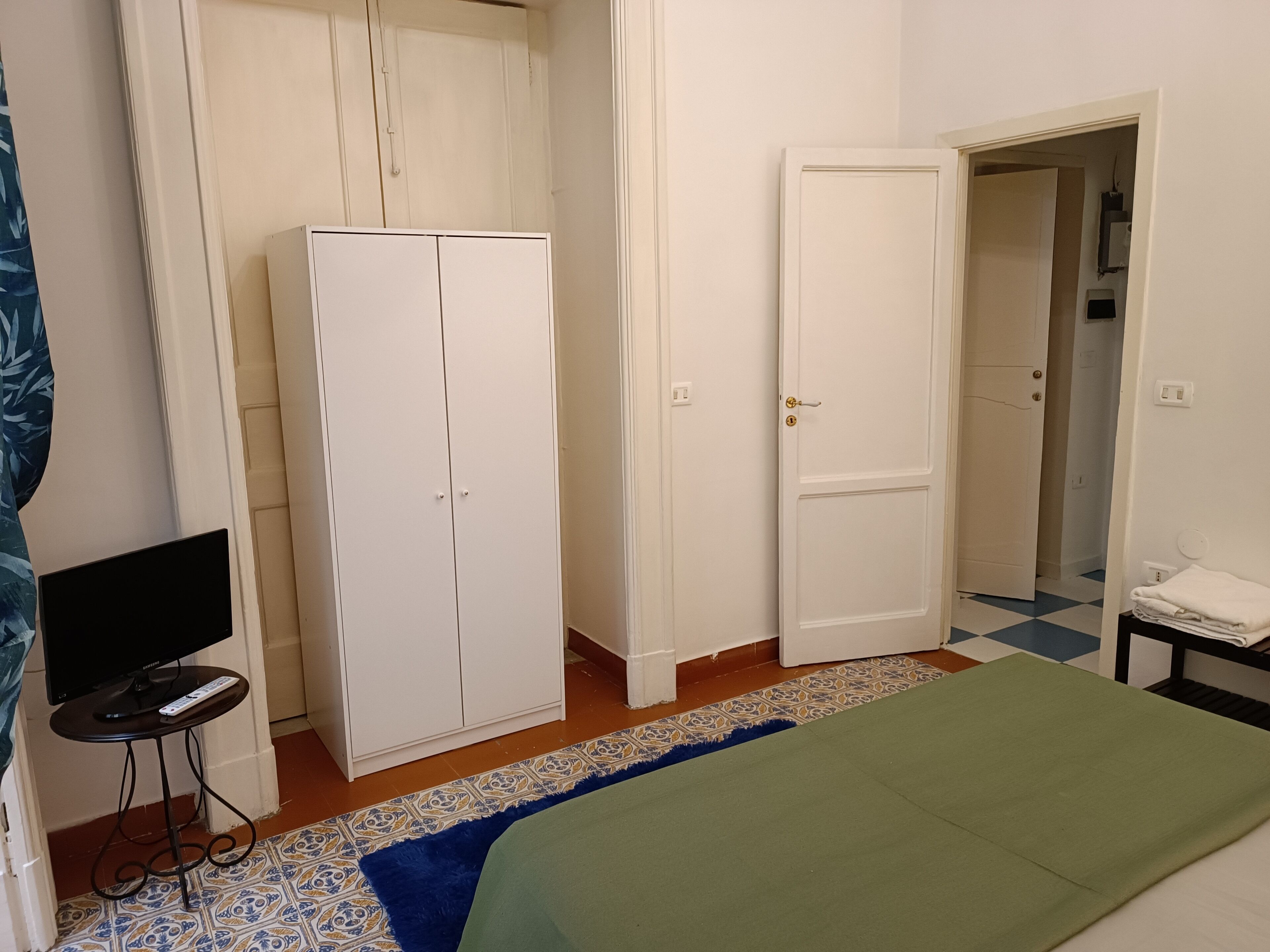 A bedroom with a bed, a wardrobe, a television on a small table, and a bathroom door.