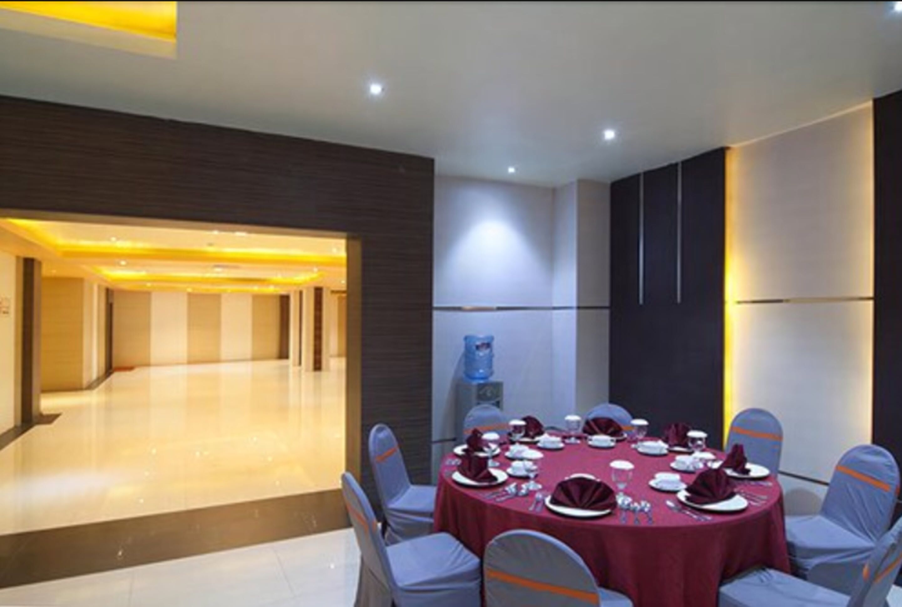 A conference room with a round table set for a meeting, equipped with chairs and a water dispenser.