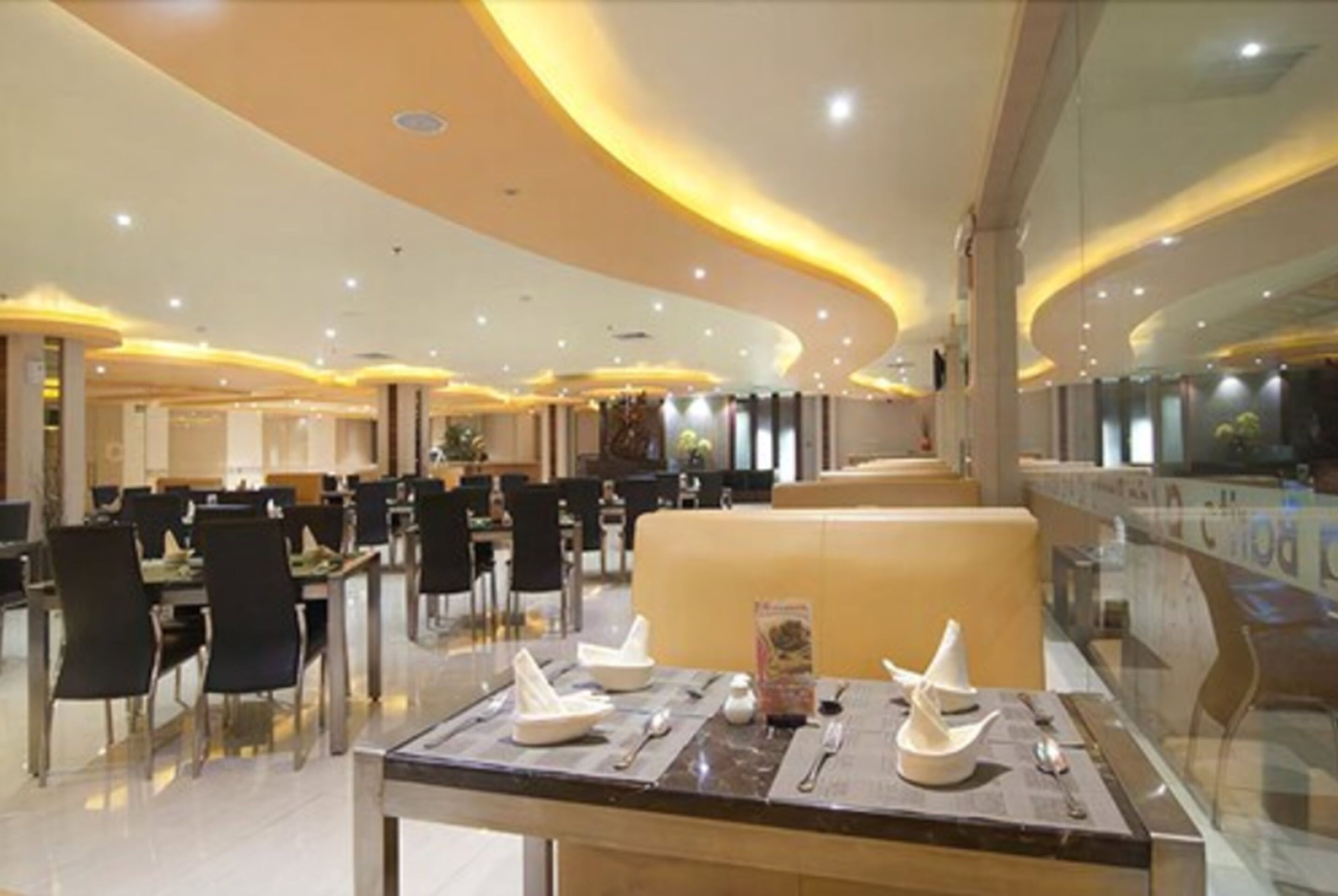 A spacious dining area with multiple tables and chairs, a central seating area, and a modern ceiling design.