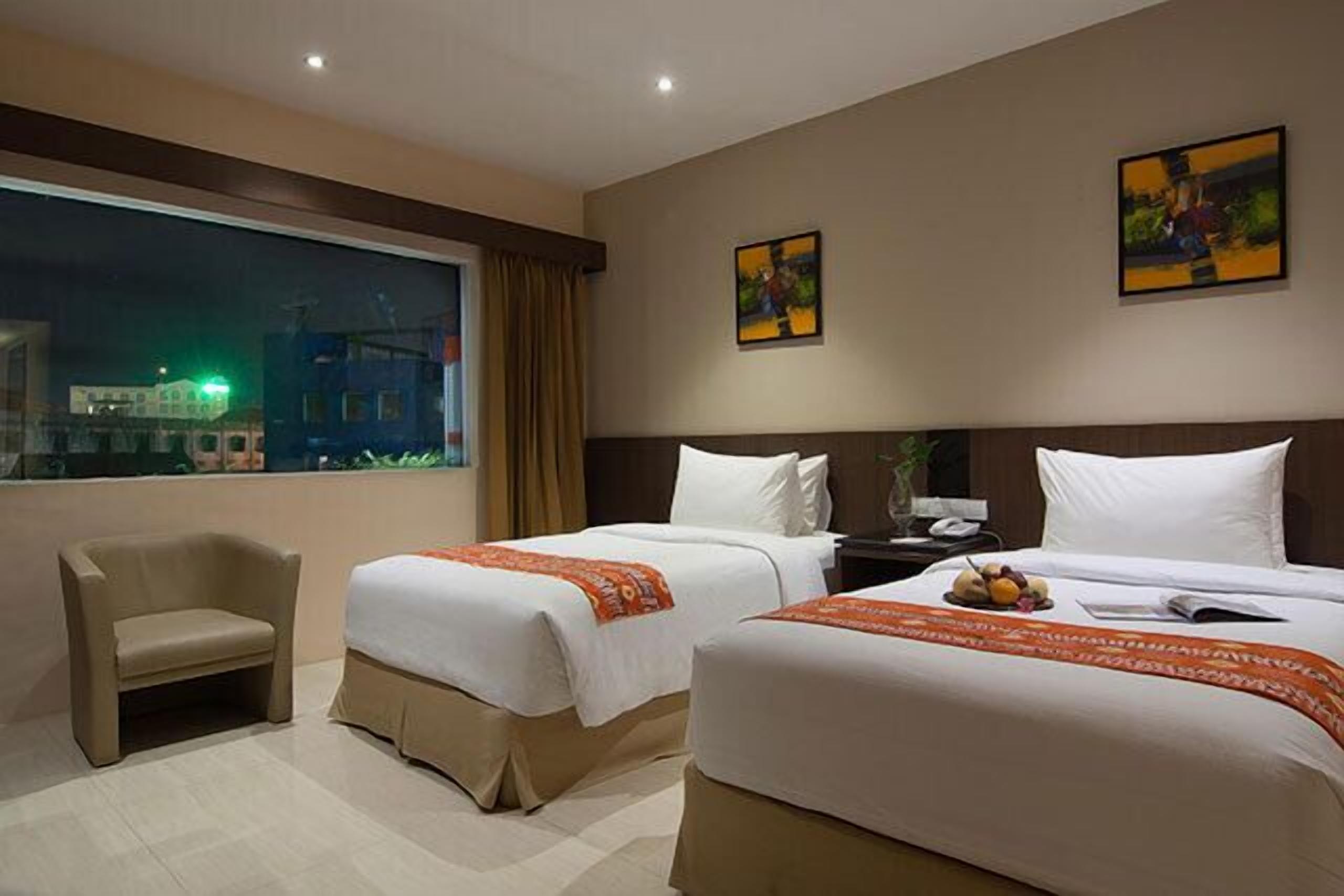 A hotel room with two beds, a chair, a nightstand, and artwork on the walls.