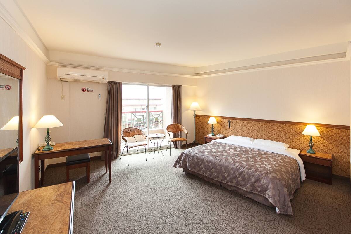 A hotel room with a bed, desk, chairs, and a window with curtains.