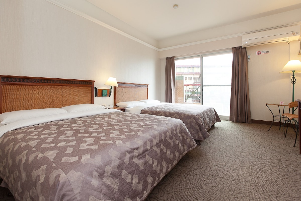 A hotel room with two beds, a desk, a chair, and a window with curtains.