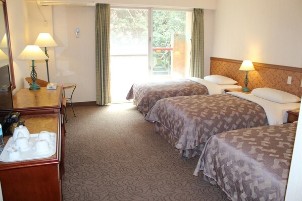A hotel room with two beds, a desk with a lamp, a chair, and a television.
