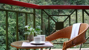 A wicker chair and table on a balcony with a view of dense greenery. - Hoya Hot Springs Hotel (Taimali)