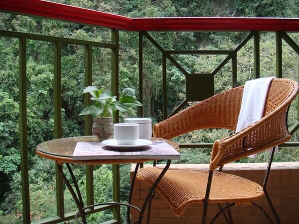A wicker chair and table on a balcony with a view of dense greenery.