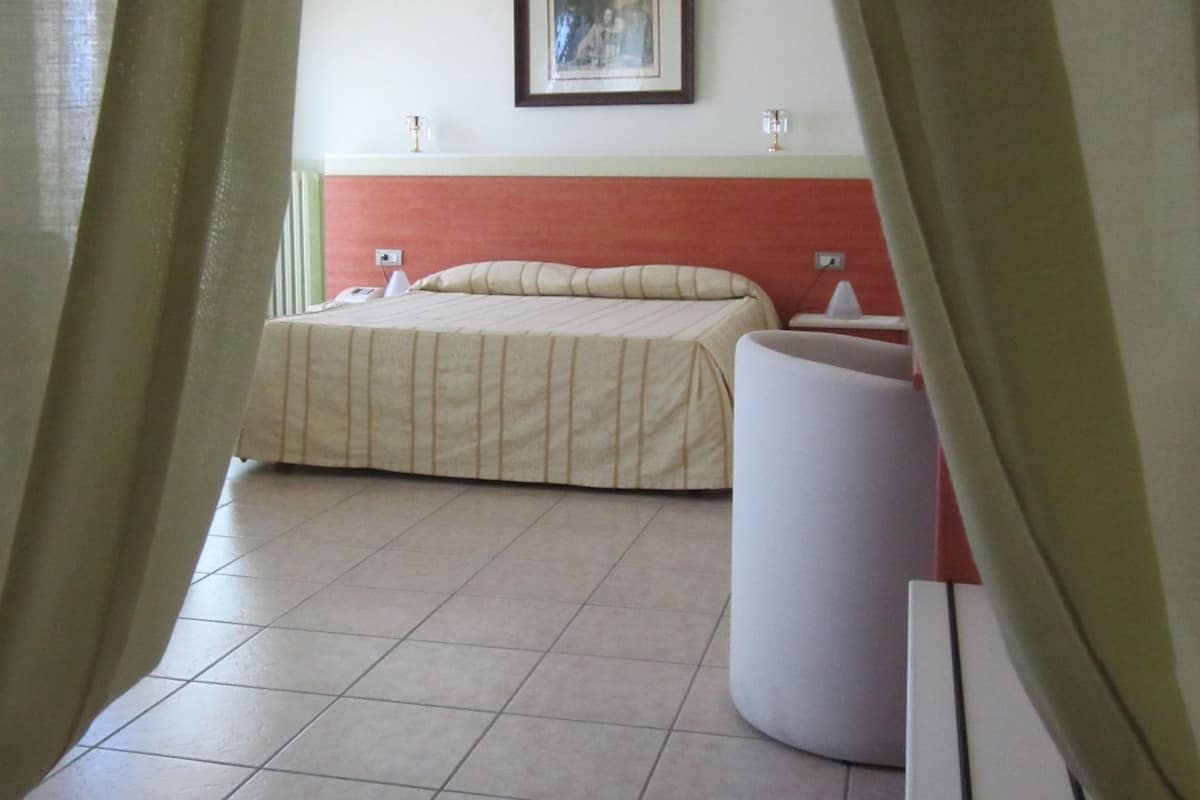 A hotel room with a bed, a bedside table, a chair, and a wall-mounted picture.