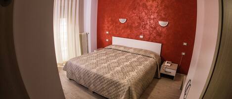 A bedroom with a bed, a nightstand, a telephone, and a wall-mounted light fixture.