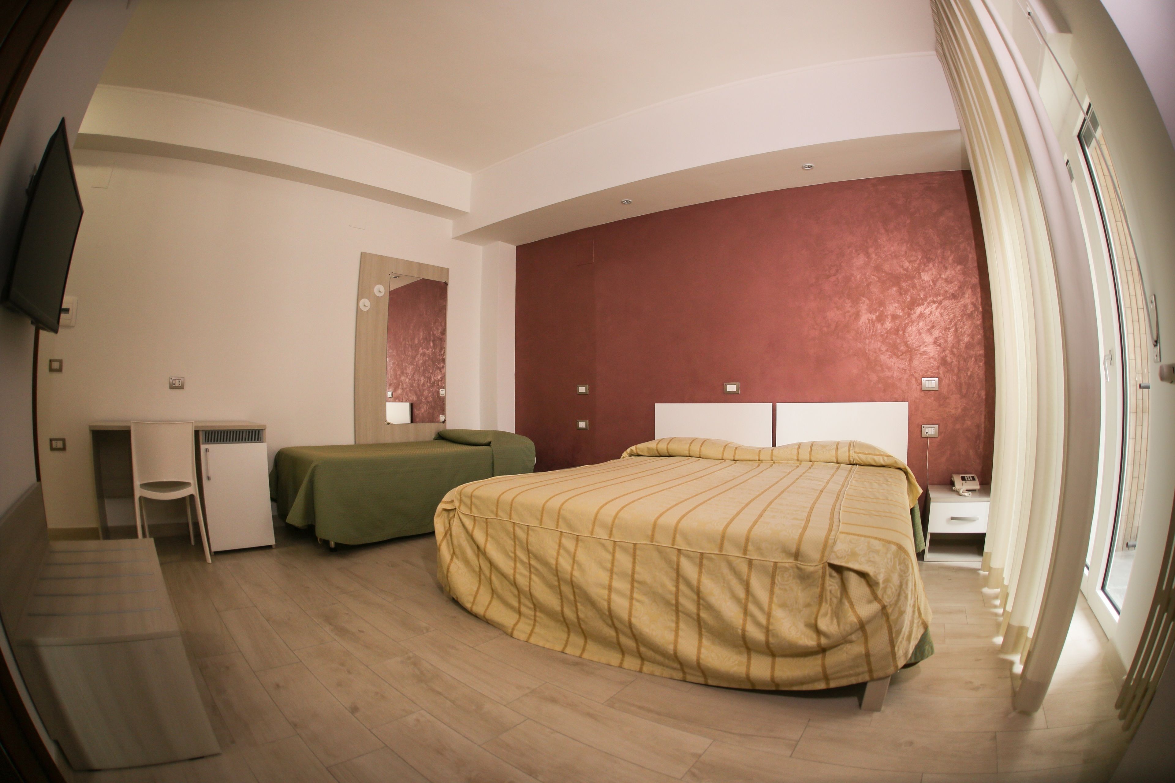 Habitación de hotel con cama, escritorio, silla, televisor y una pared roja decorativa.