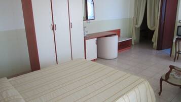 Quarto com cama, guarda-roupa, escrivaninha, cadeira e banheiro visível por uma porta aberta.