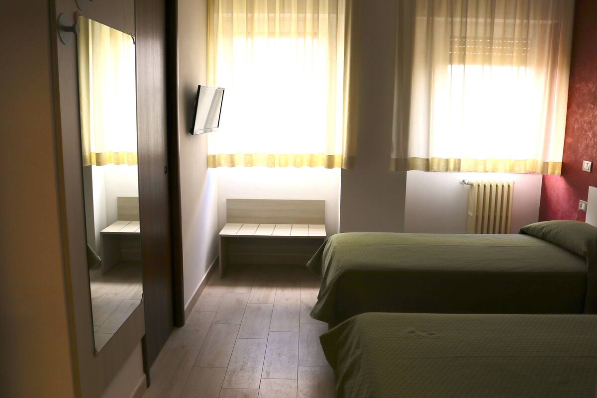 A hotel room with two beds, a bench, a radiator, and a mirror.