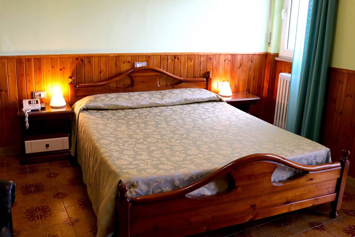 A wooden-framed bed with a floral bedspread, two bedside tables with lamps, a nightstand with a telephone, and a radiator.