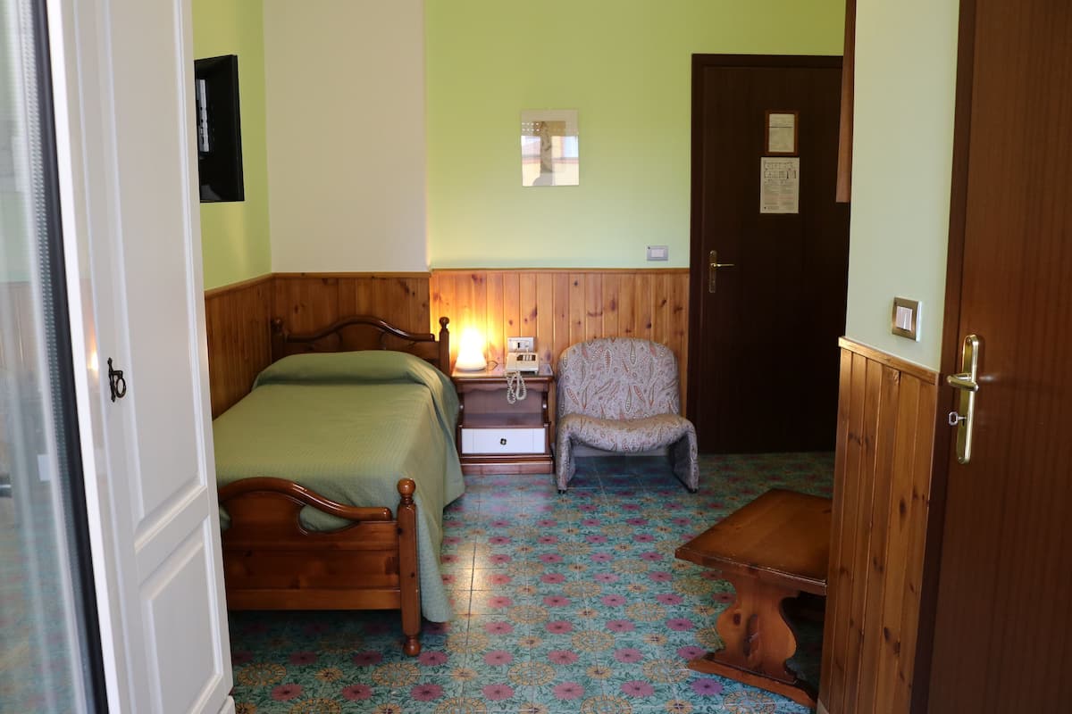 A bedroom with a wooden bed, a nightstand, a chair, and a door.