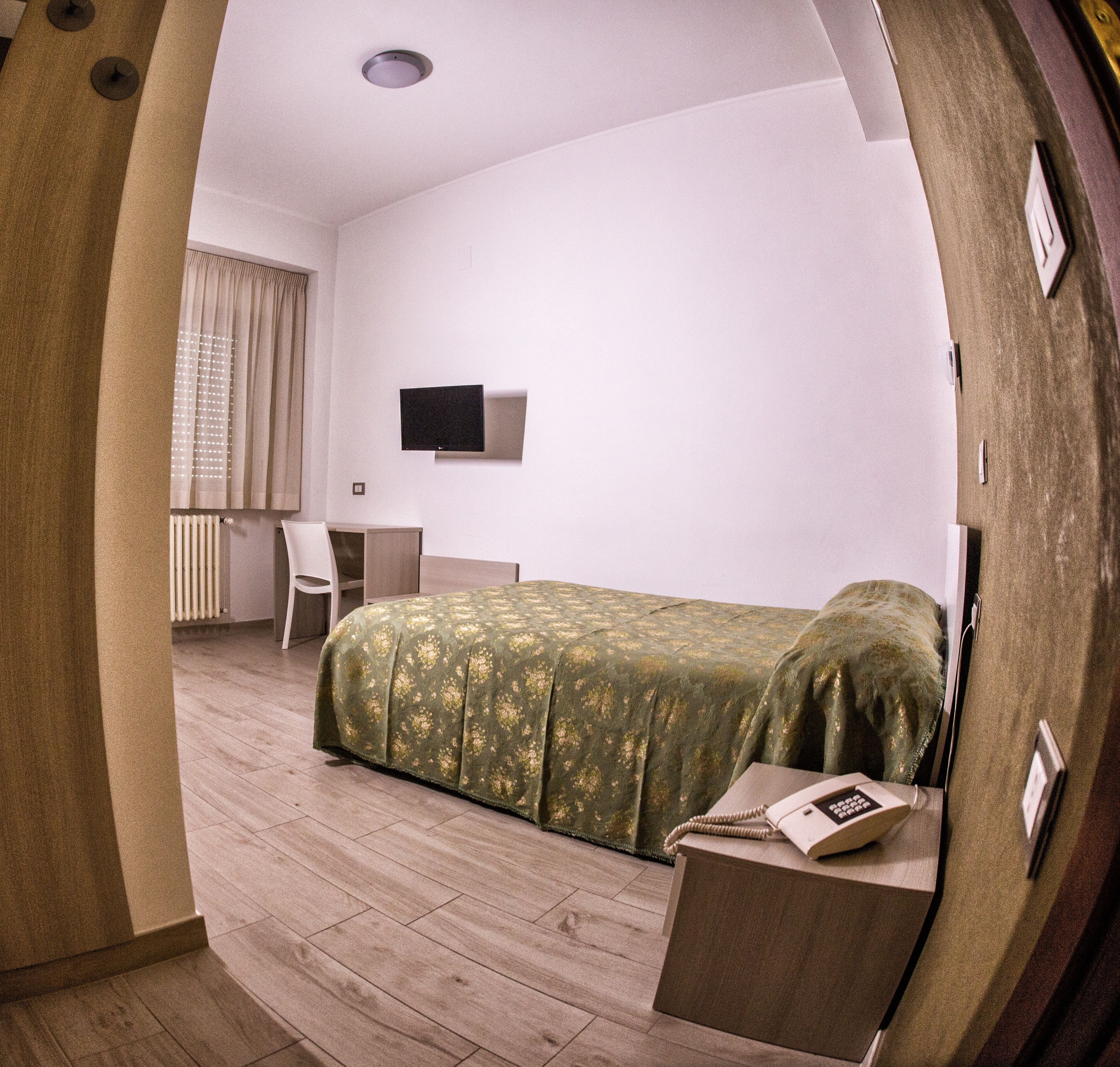 A bedroom with a bed, a desk, a chair, a TV, and a radiator.