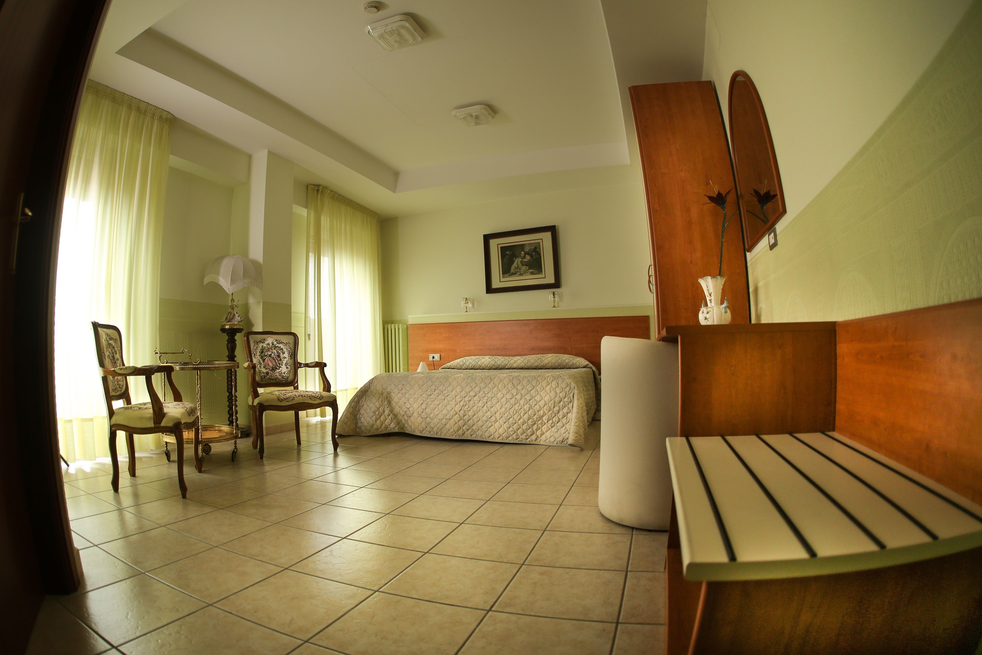 A hotel room with a bed, two chairs, a table, a bedside table, a mirror, and a picture on the wall.