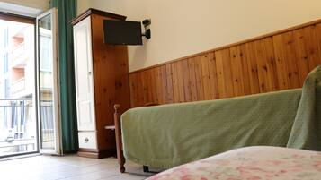 Ein Zimmer mit einem Bett, einem Holzschrank, einem an der Wand montierten Fernseher und einer Glastür zum Balkon.
