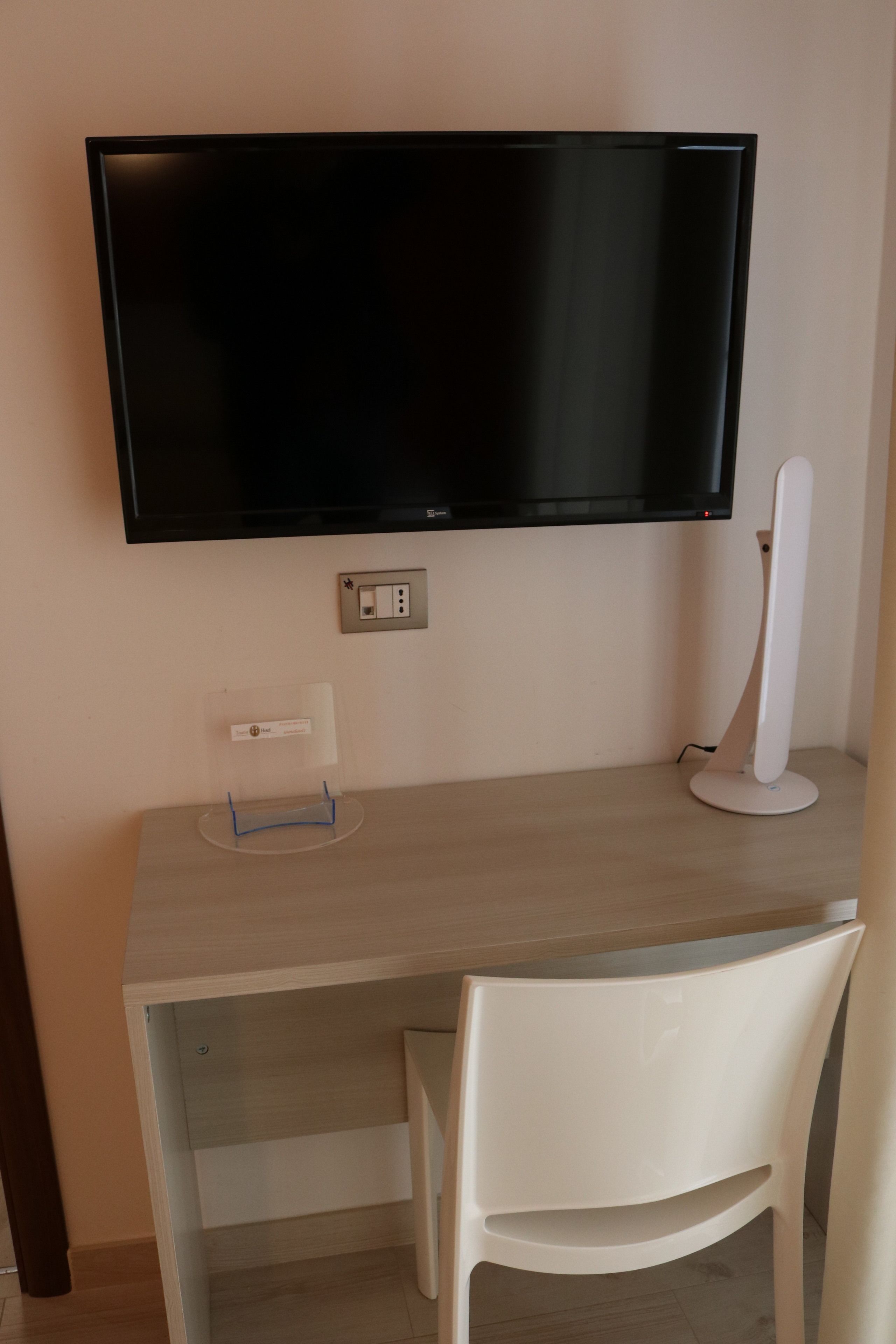 A modern office desk with a flat-screen monitor, a white chair, and a clear plastic stand.