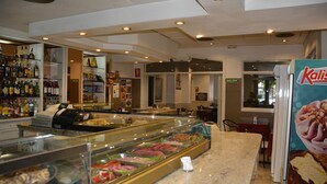 A deli counter with a glass display case filled with various meats and cheeses, a cash register, and a sign for 'SALIDA'. - Hotel Casa Emilio (Murcia)