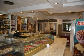 A deli counter with a glass display case filled with various meats and cheeses, a cash register, and a sign for 'SALIDA'.