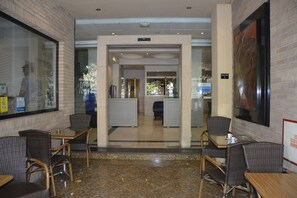 A hotel lobby with wicker furniture, a glass coffee table, and a tiled floor.
