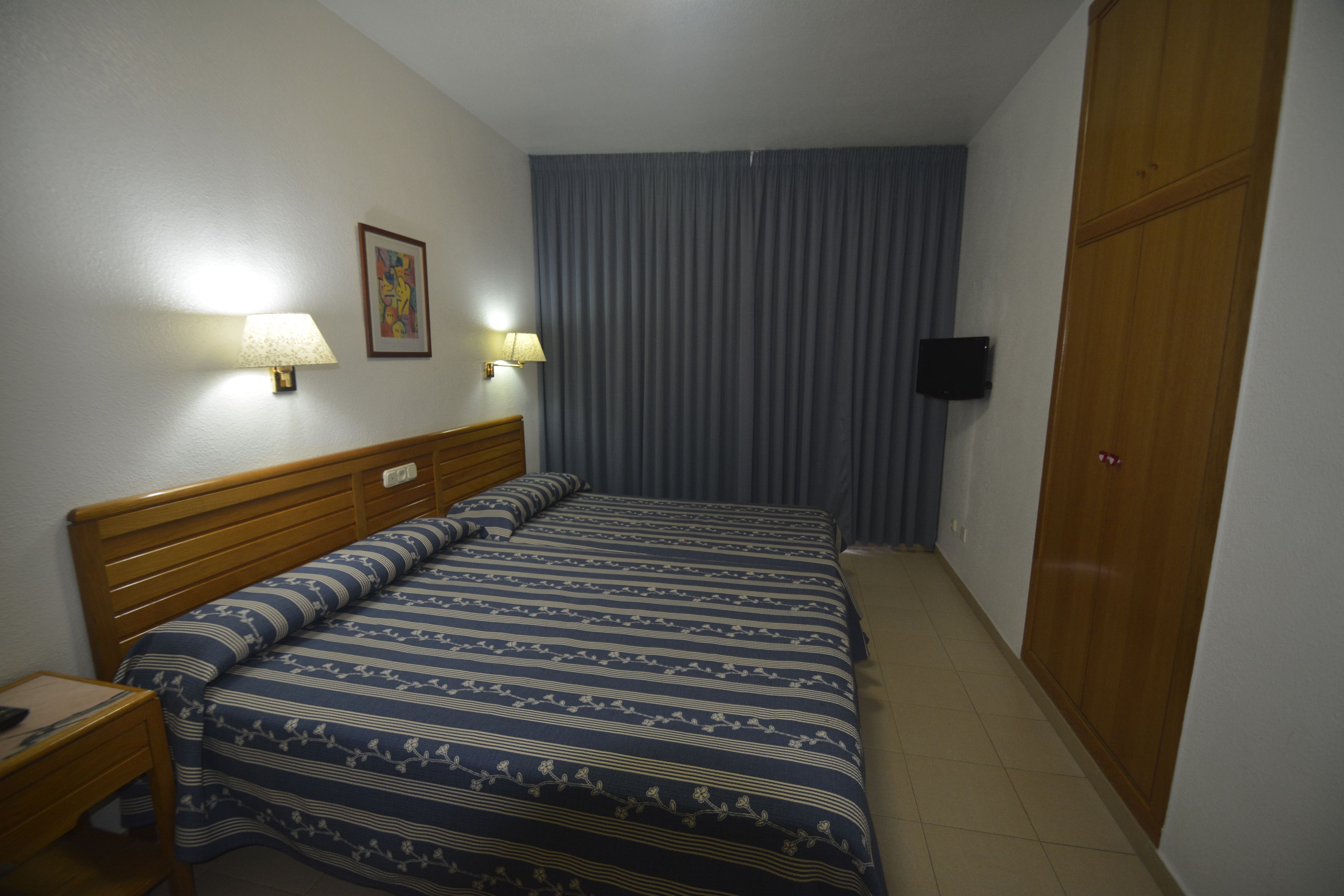 Una habitación de hotel con una cama, dos lámparas de noche, un televisor montado en la pared y un armario.
