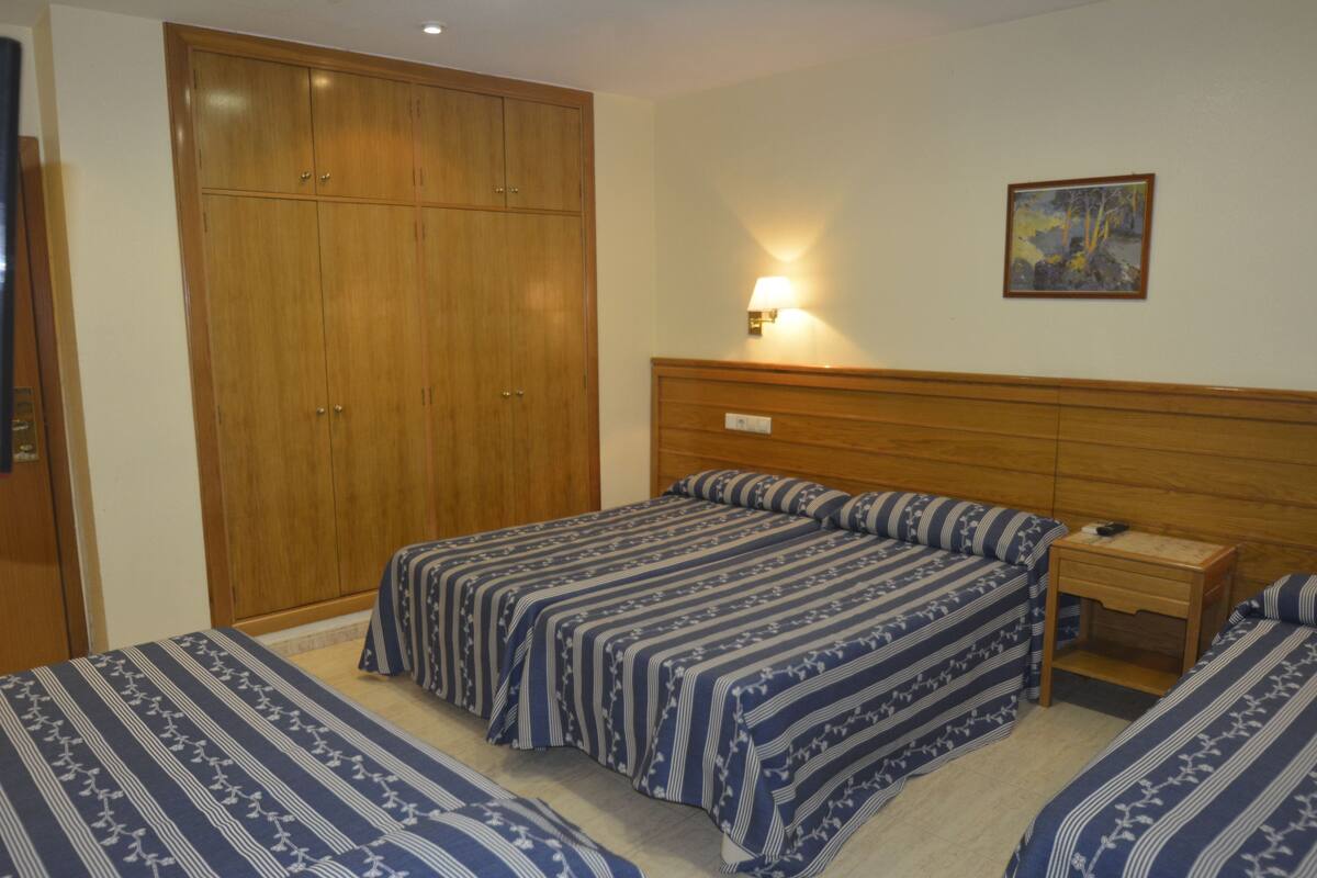 A bedroom with a large wardrobe, a bed with matching bedding, a bedside table, and a wall-mounted lamp.