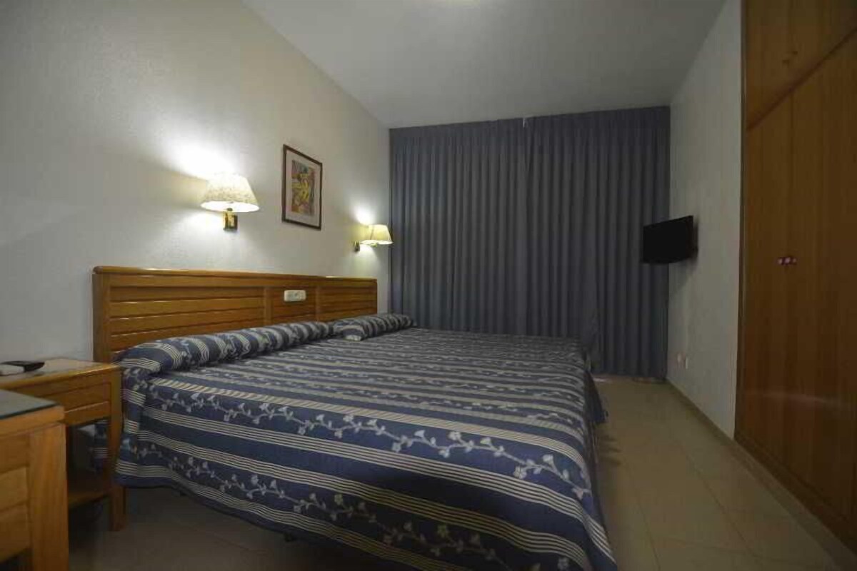 Une chambre d’hôtel avec un lit en bois, deux lampes de chevet, un téléviseur à écran plat et une armoire.