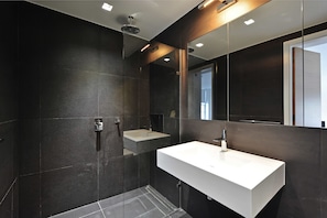 A modern bathroom with dark tiles, a white sink, and a large mirror.