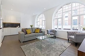A modern living room with a grey sofa, a glass coffee table, and a grey armchair.