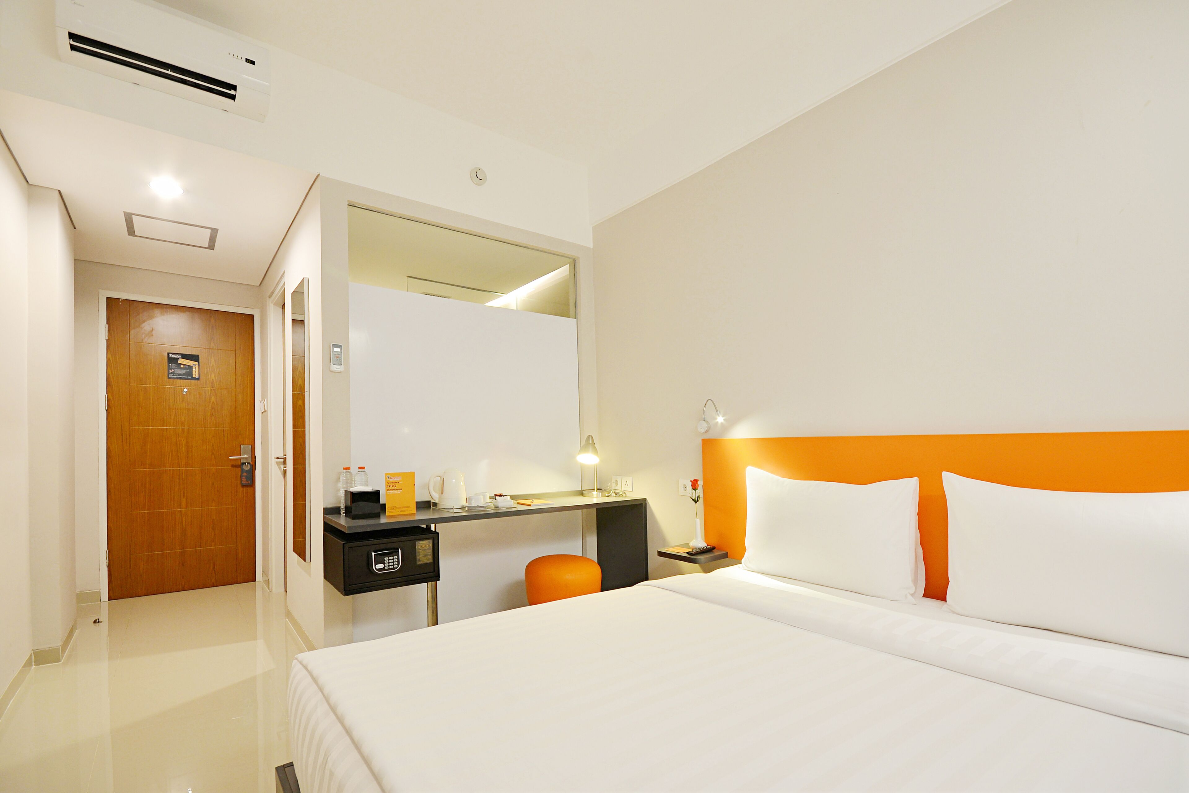 A hotel room with a bed, a desk, a chair, a nightstand, and a mirror.