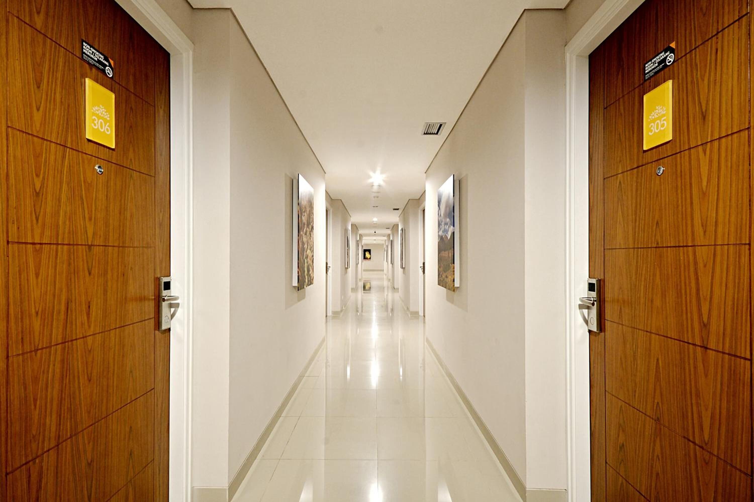Pasillo de hotel con puertas de madera, números 306 y 305, y un suelo limpio y reflectante.