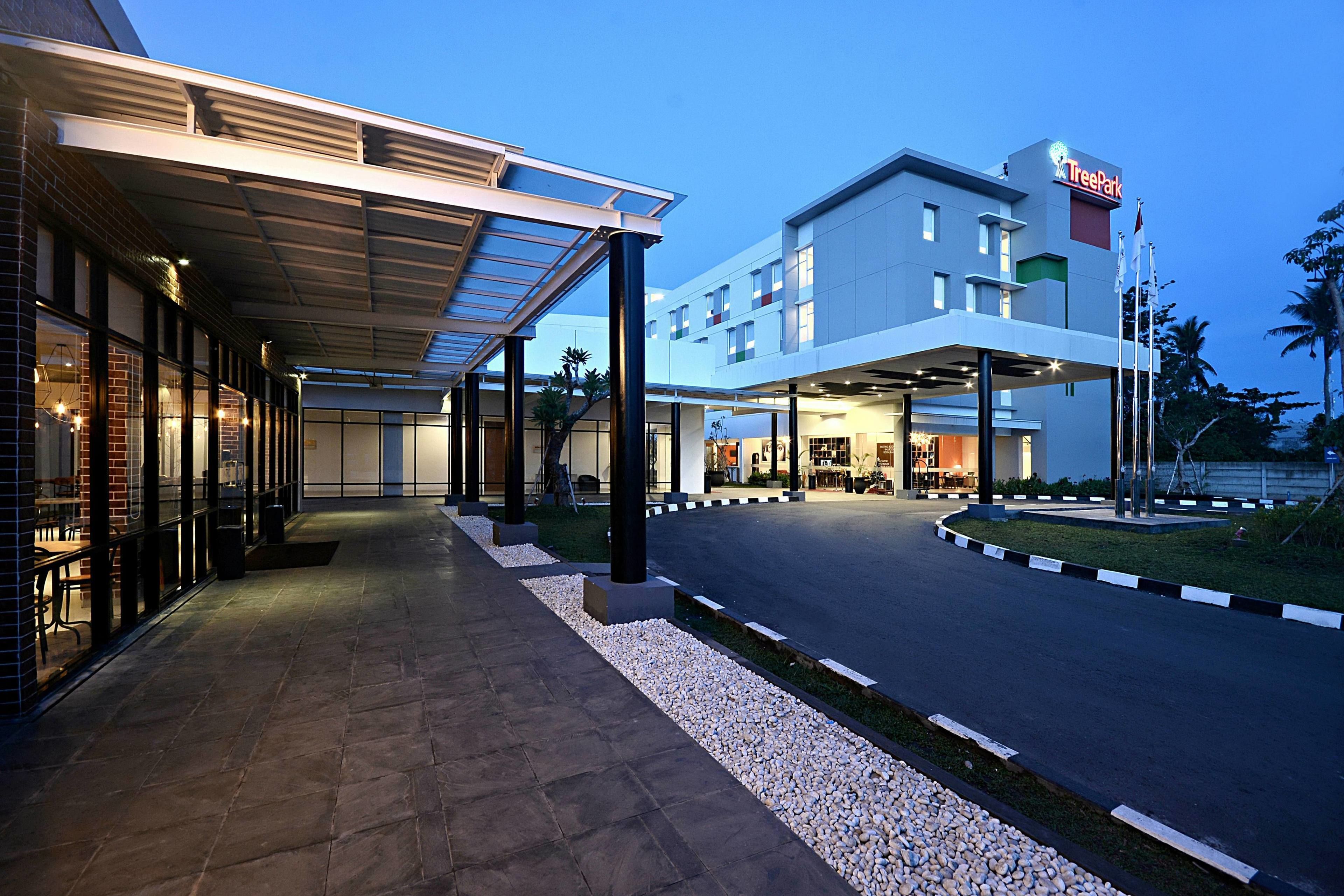 Entrada de hotel con un paseo techado, zona de estacionamiento y un edificio con el letrero 'TreePark'.