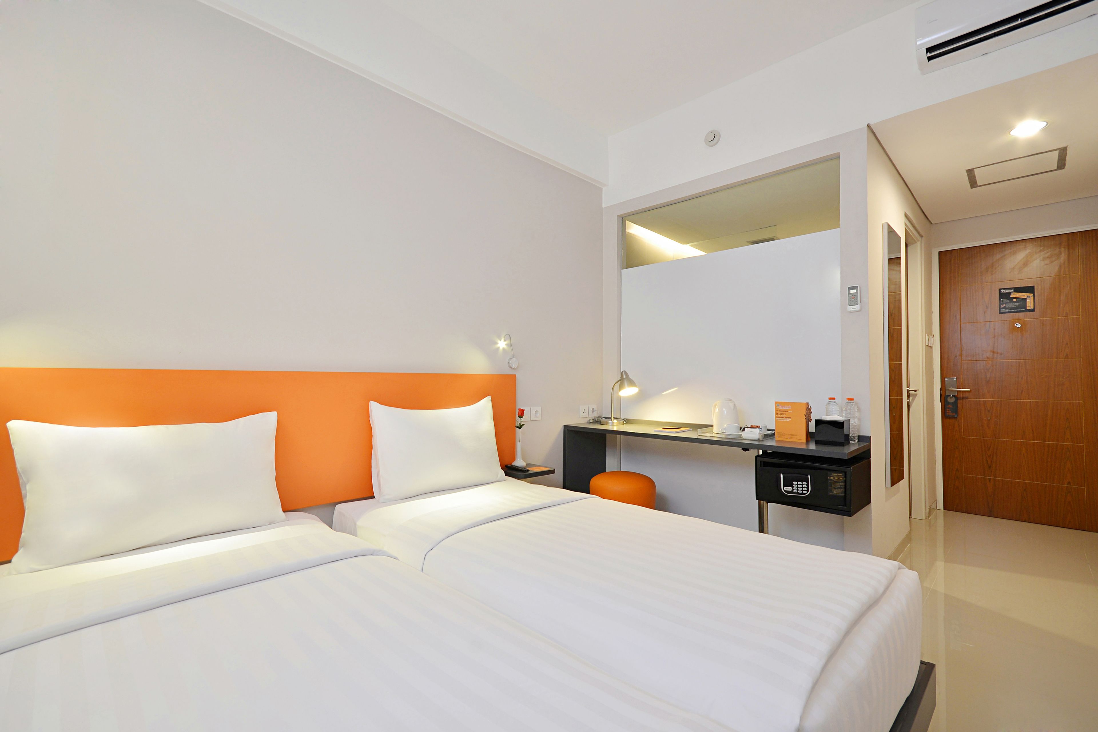 Een hotelkamer met twee bedden, een bureau met een computer, een spiegel en een deur.
