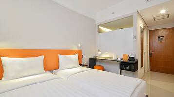 Een hotelkamer met twee bedden, een bureau met een computer, een spiegel en een deur.