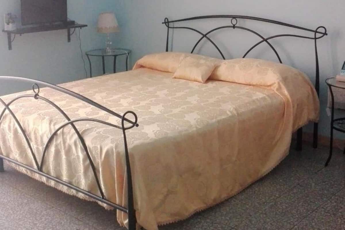 Un lit simple avec un cadre en métal et une couvre-lit beige, dans une pièce aux murs bleu clair.